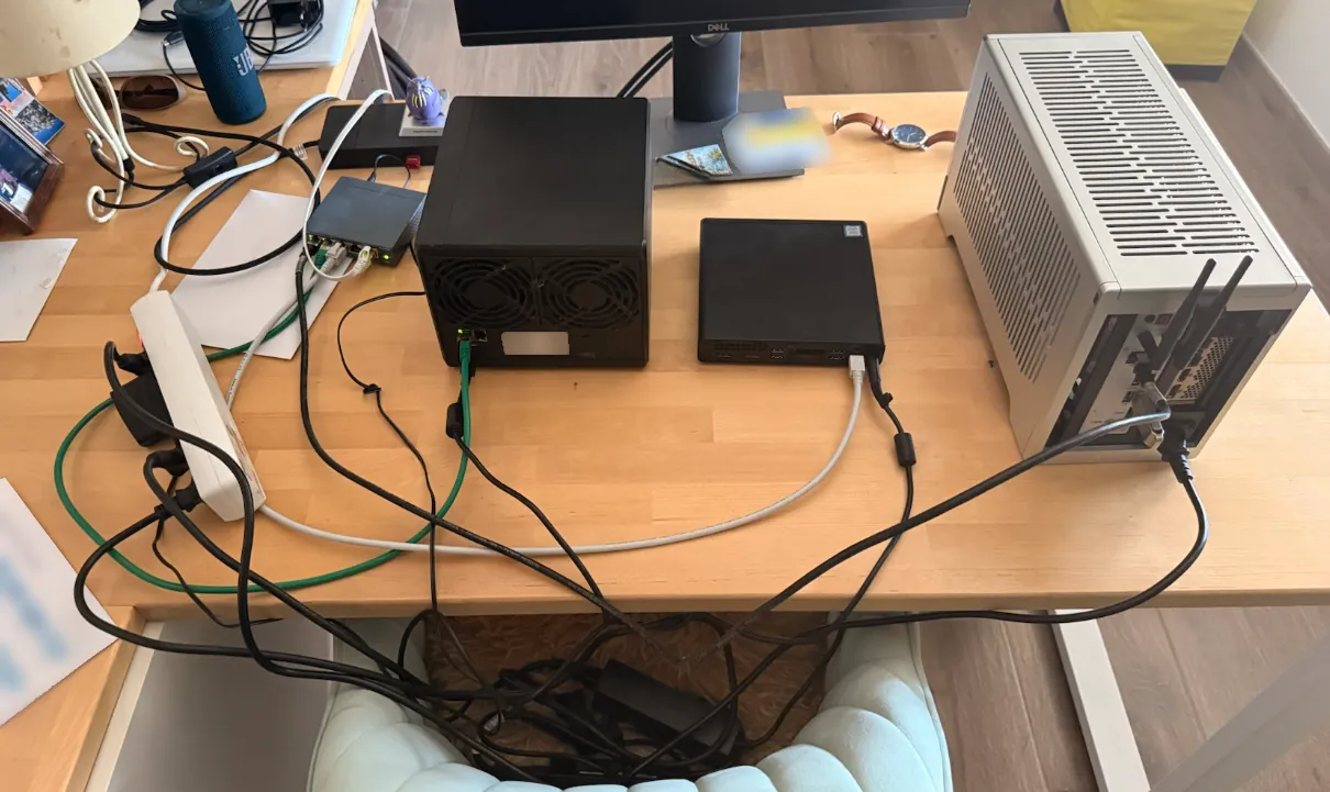Bureau avec l’installation temporaire : au centre un NAS Synology noir à 4 baies, à sa droite un mini-PC HP ProDesk, plus à droite le PC MINI-LEO dans un boîtier Fractal Design Terra gris, et à gauche du NAS un petit switch TP-Link.