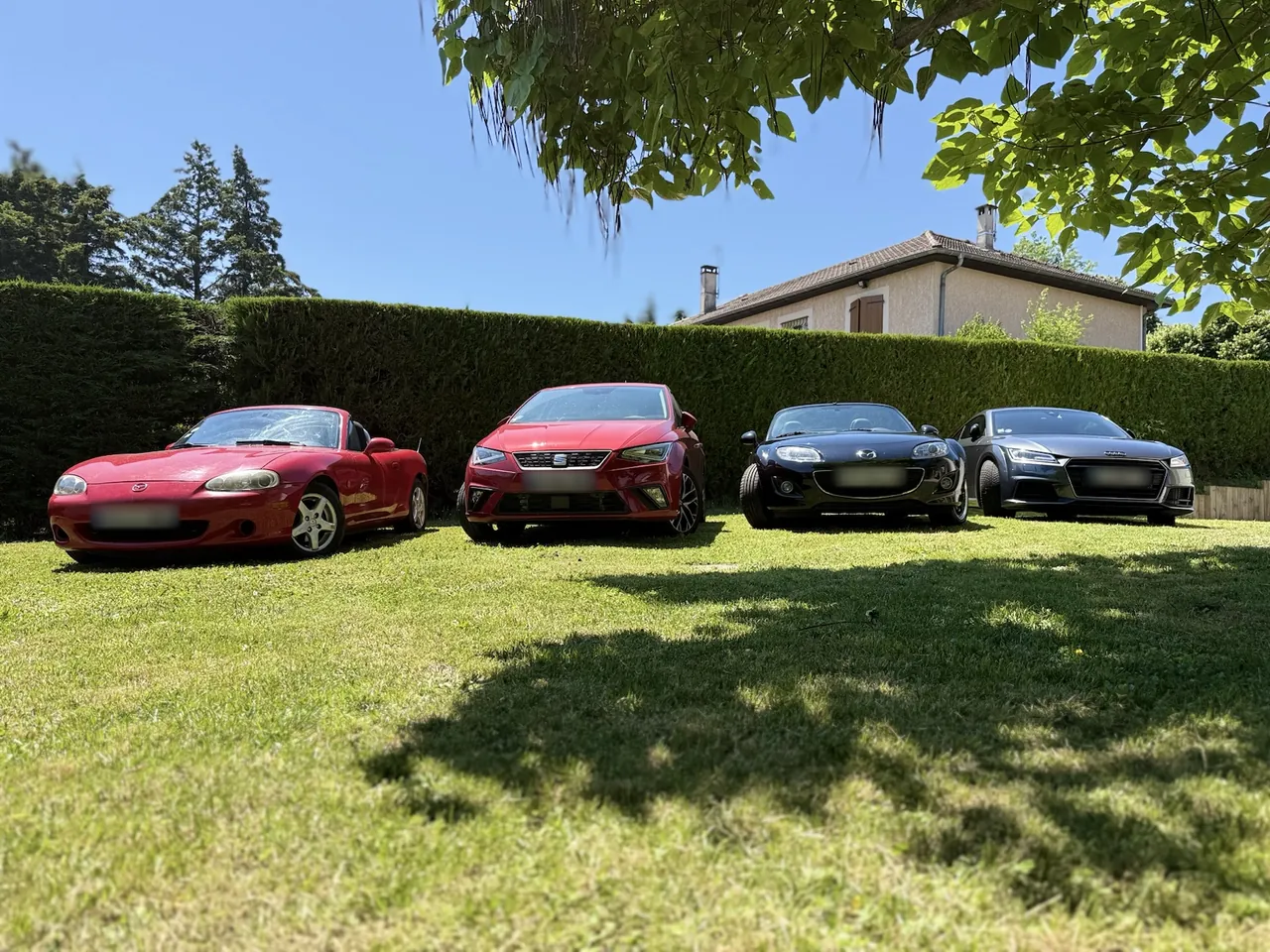 Quatre voitures alignées sur l'herbe, dont deux Mazda MX-5 : une NB rouge et une NC noire.