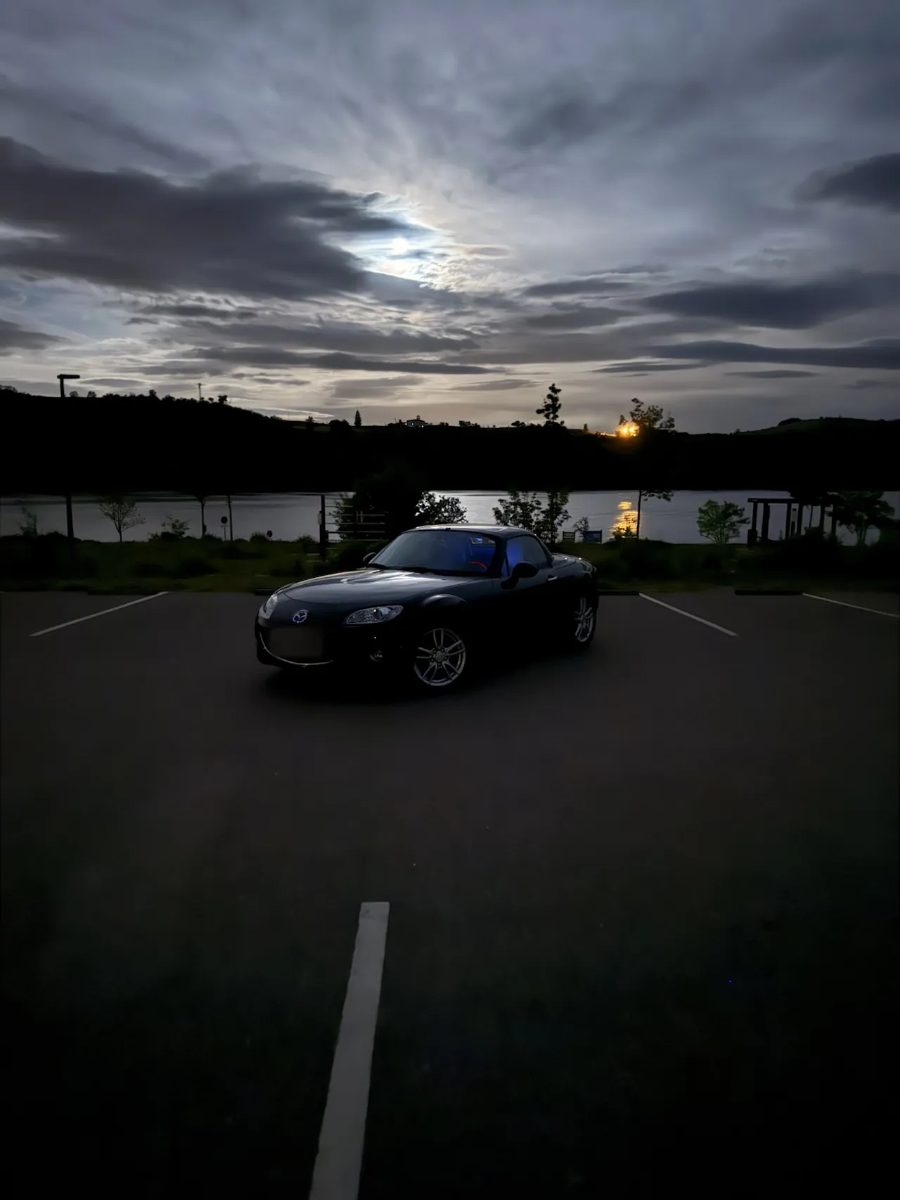 Mazda MX-5 NC noire de trois-quarts au bord du lac de Villerest au crépuscule.