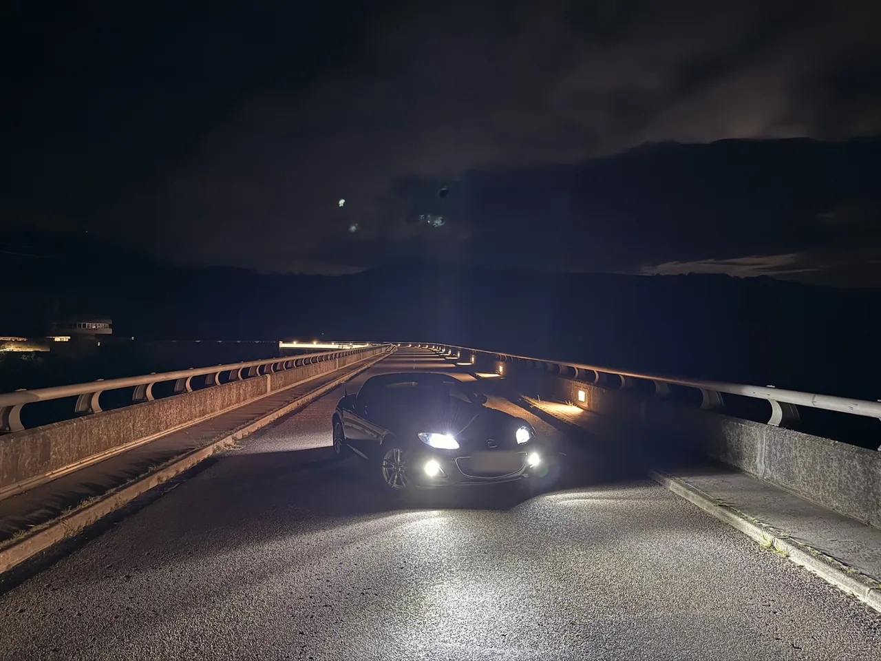 Mazda MX-5 NC phares allumés, de nuit sur le barrage de Villerest, en plan plus large.